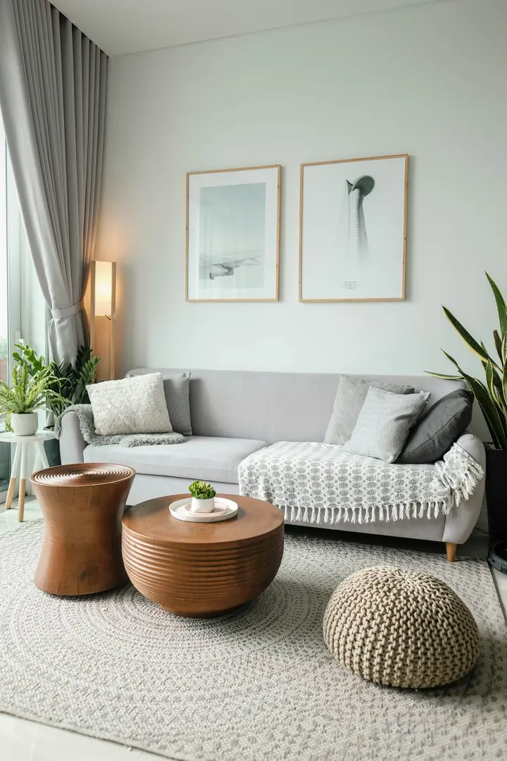 Ljust vardagsrum med grå soffa, runda sidobord och stort fönster i dagsljus