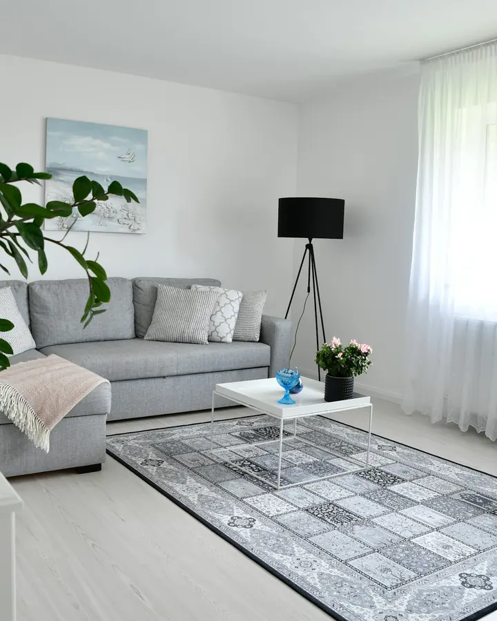Ljust vardagsrum med grå soffa, stor krukväxt och vita gardiner
