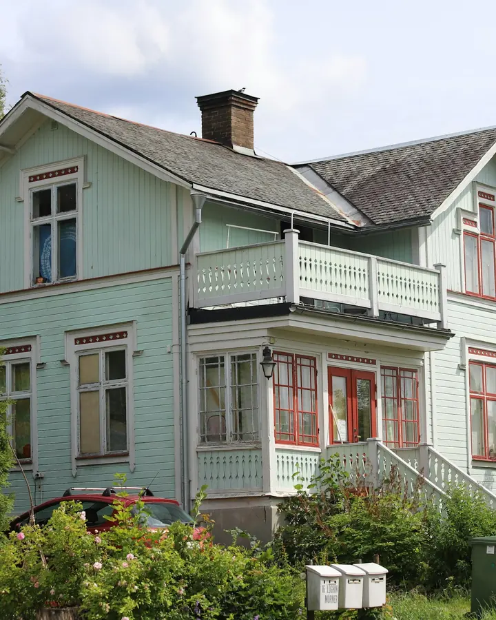 Ljusgrön trävilla med vita knutar och trädgård en sommardag