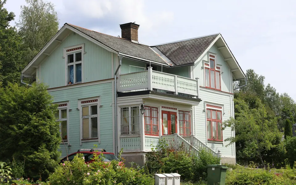 Ljusgrön trävilla med vita knutar och trädgård en sommardag